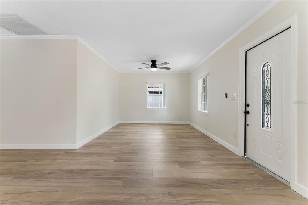 An empty room features light wood-look flooring, a ceiling fan, and a white front door — 4727 W BAY VISTA AVENUE, TAMPA, FL