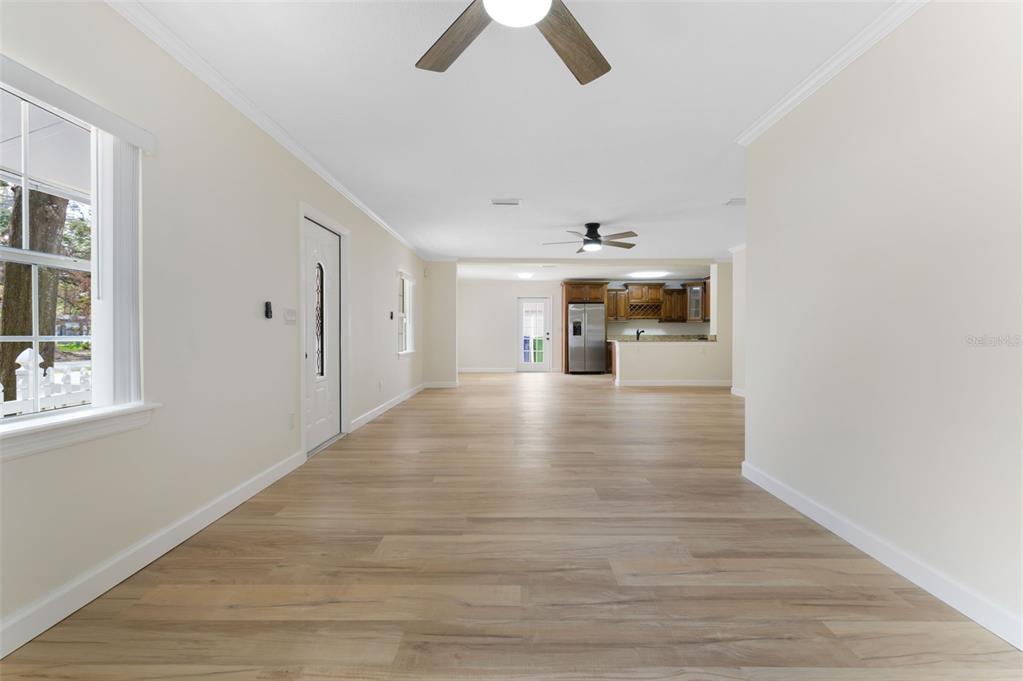 An open-concept living area with light wood-look flooring leads toward a kitchen with wooden cabinets — 4727 W BAY VISTA AVENUE, TAMPA, FL