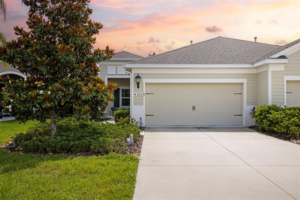 A beige single-story house features a two-car garage, a concrete driveway, and a large tree — 4524 DEEP CREEK TERRACE, PARRISH, FL