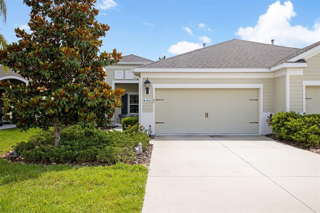 A beige house exterior features a two-car garage, a concrete driveway, and a large tree — 4524 DEEP CREEK TERRACE, PARRISH, FL