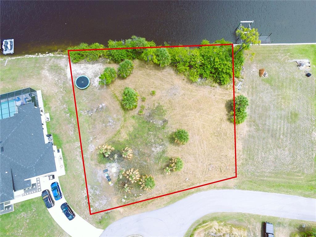 An aerial view shows a vacant, grassy waterfront lot outlined in red — 13303 IRWIN DRIVE, PORT CHARLOTTE, FL