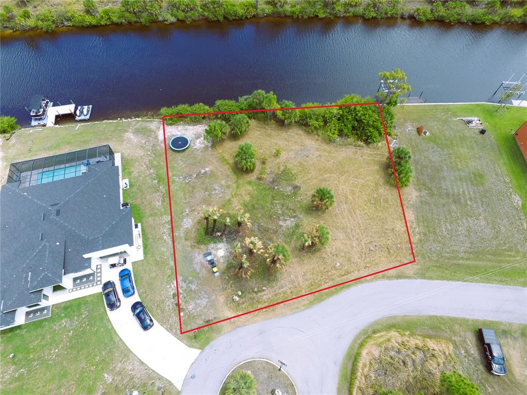 An aerial view shows a vacant waterfront lot outlined in red next to a house — 13303 IRWIN DRIVE, PORT CHARLOTTE, FL