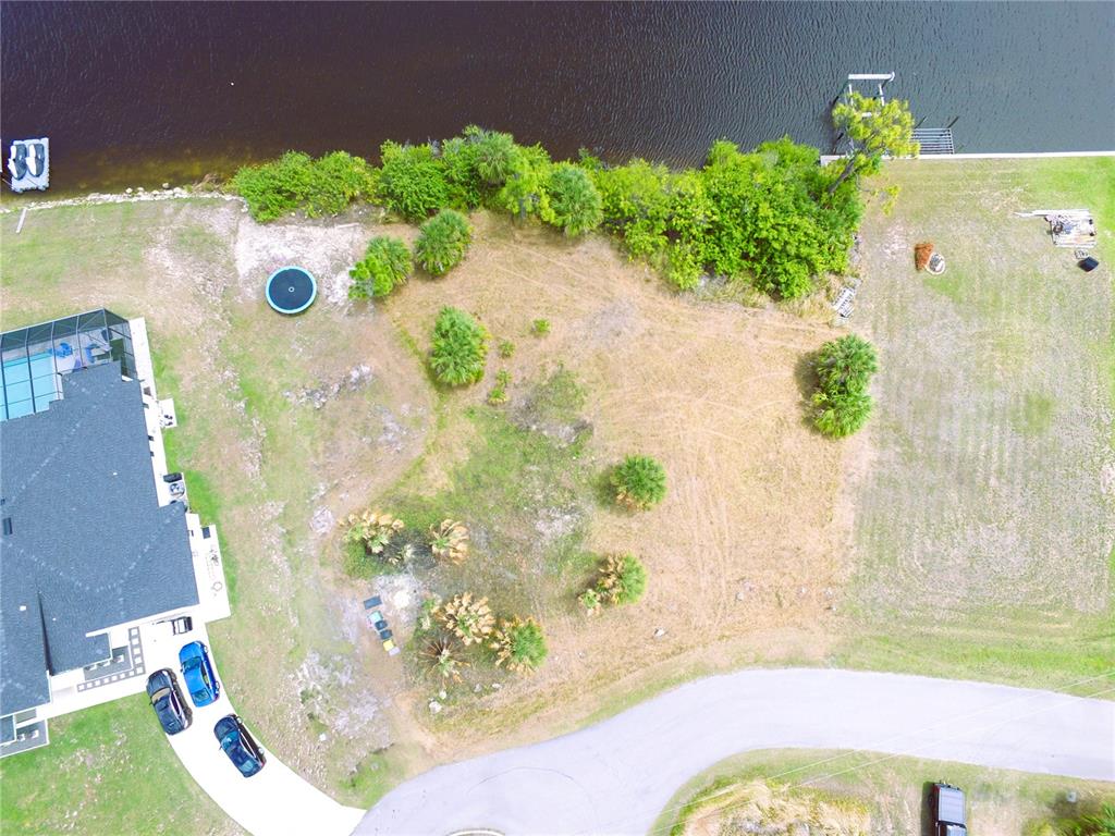 An aerial view shows a vacant waterfront lot next to a house with a pool — 13303 IRWIN DRIVE, PORT CHARLOTTE, FL