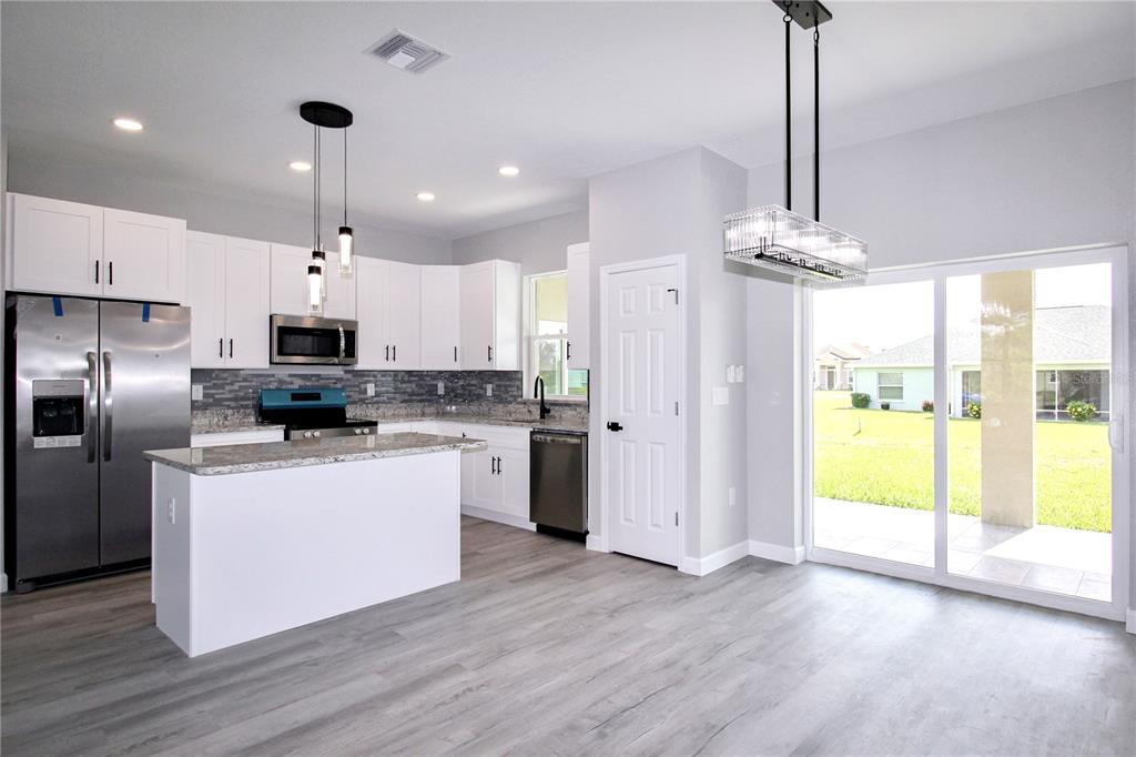 A modern kitchen features white cabinets, stainless steel appliances, a granite island, and sliding doors — 4631 MIGNON DRIVE, SEBRING, FL