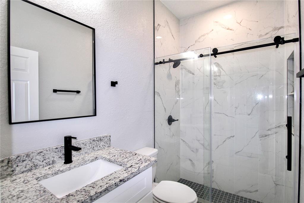 A modern bathroom features a granite vanity, black fixtures, and a glass-enclosed marble tile shower — 4631 MIGNON DRIVE, SEBRING, FL