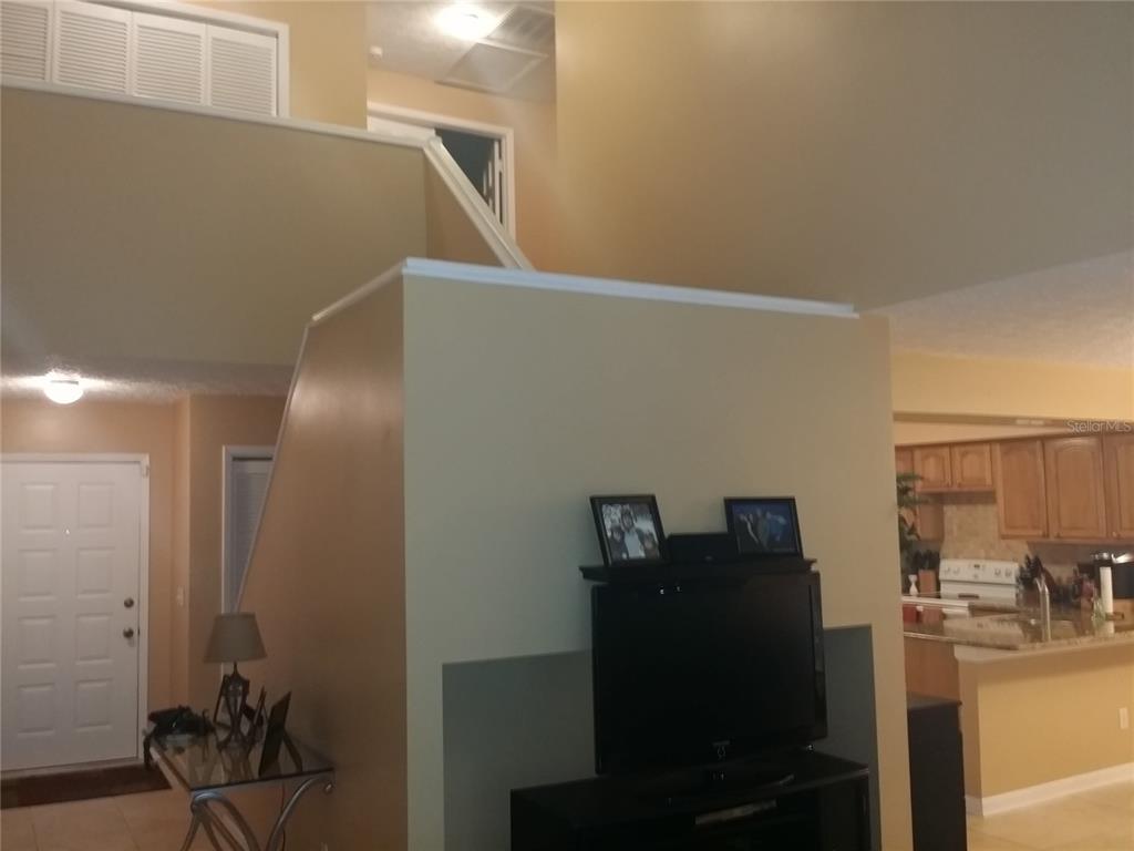 A view of a living room with a television, a staircase, and an open kitchen — 4012 CIRCLEWOOD COURT, TAMPA, FL