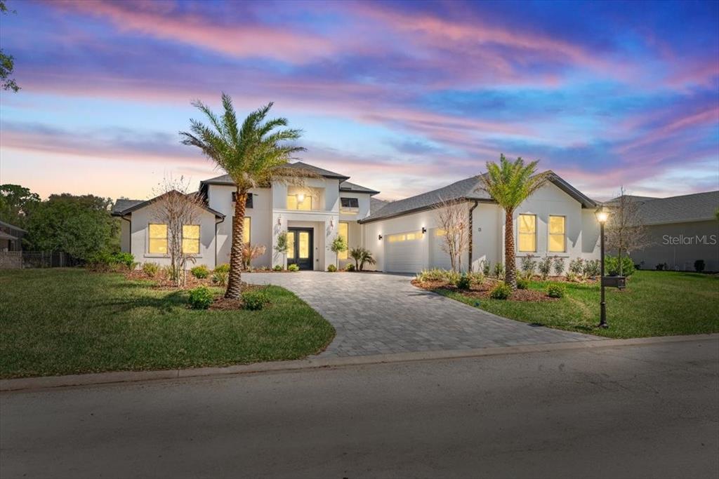 A modern white house with a paved driveway and palm trees under a sunset sky — 13 OLD OAK DRIVE N, PALM COAST, FL