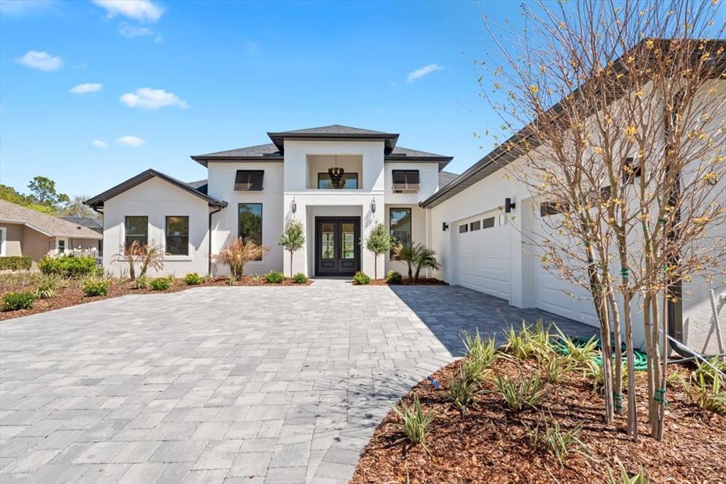 A modern white house with a paver driveway, dark window shutters, and a two-car garage — 13 OLD OAK DRIVE N, PALM COAST, FL