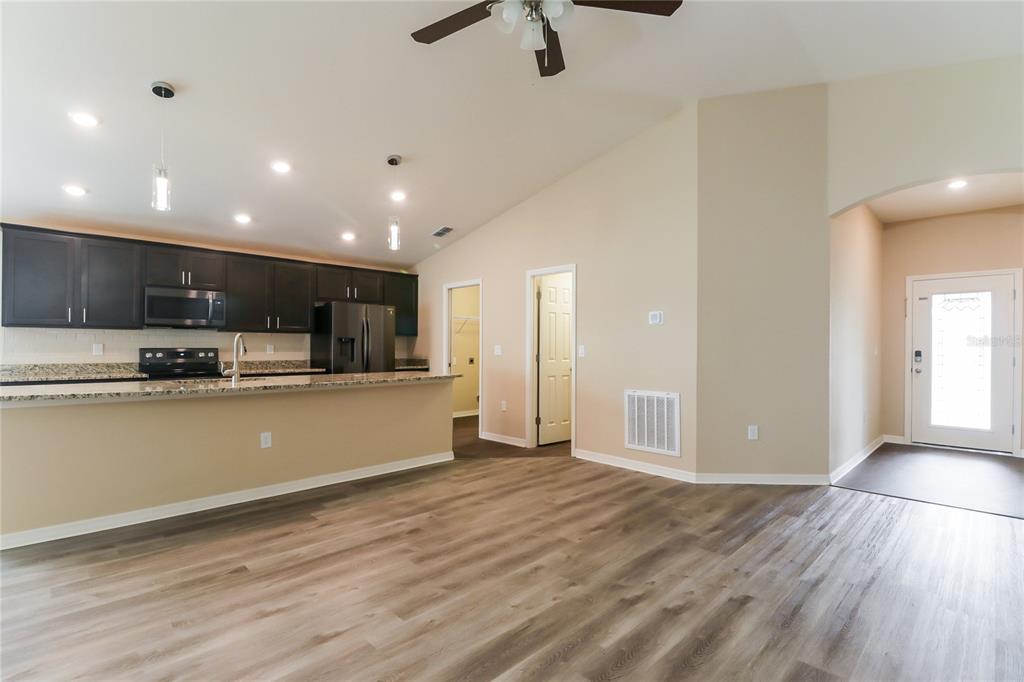 An open-concept kitchen with dark cabinets and granite countertops overlooks a living area — 6784 HANWORTH LANE, ZEPHYRHILLS, FL
