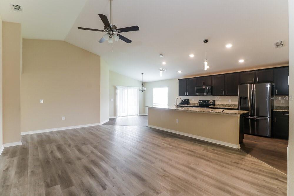 An open-concept living area features wood-look flooring, a vaulted ceiling, and a kitchen with dark cabinetry — 6784 HANWORTH LANE, ZEPHYRHILLS, FL