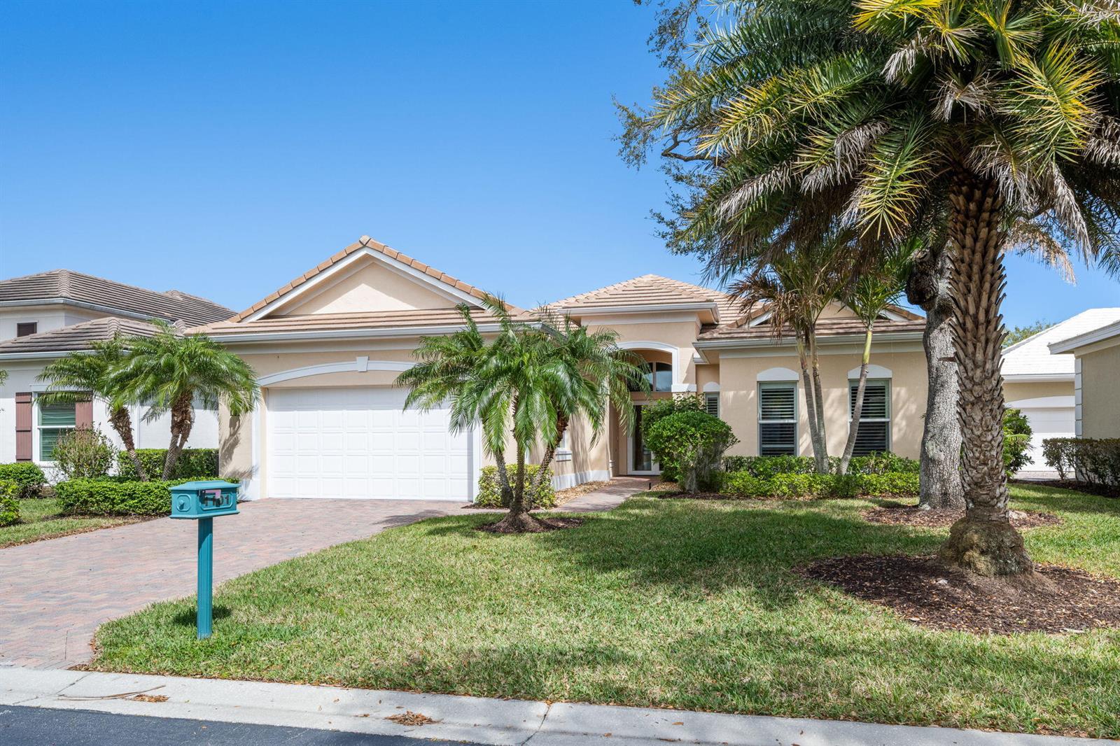 A single-story beige house with a two-car garage, palm trees, and a paved driveway — 1101 River Wind Circle, Vero Beach FL 32967, VERO BEACH, FL