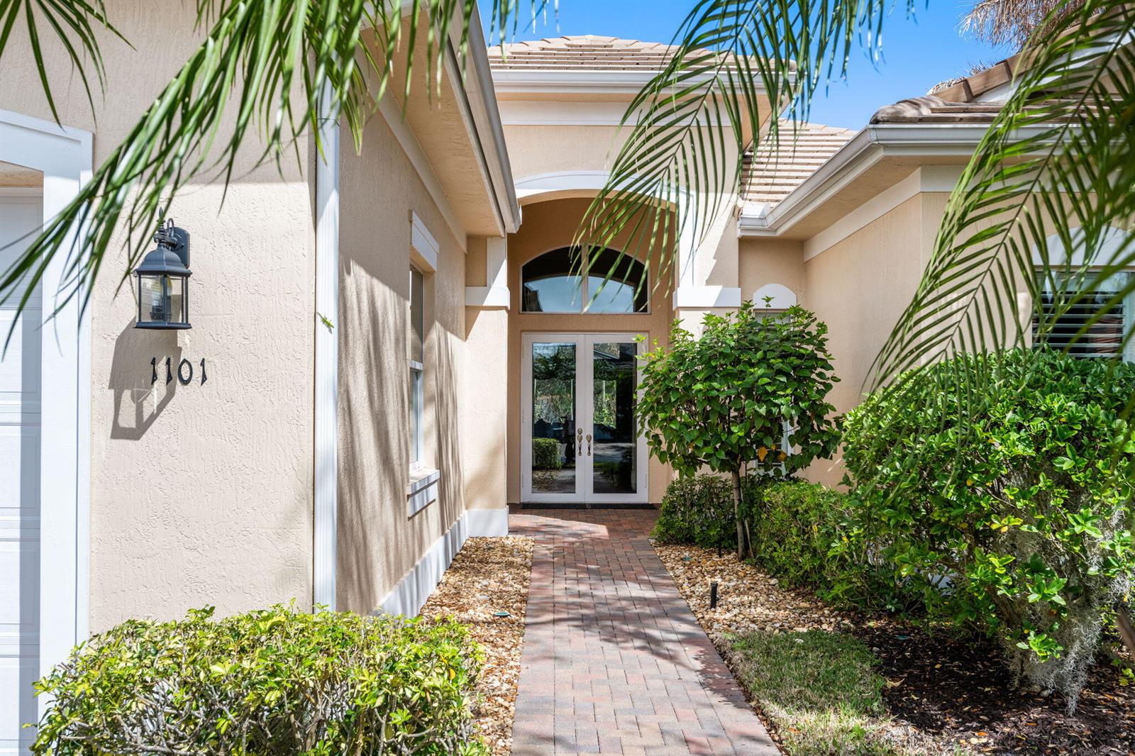 A brick walkway leads to the double front doors of a beige stucco house — 1101 River Wind Circle, Vero Beach FL 32967, VERO BEACH, FL