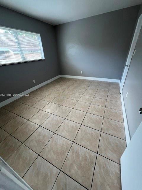 An empty bedroom with gray walls, a window with blinds, and light-colored square floor tiles — FORT LAUDERDALE, FL