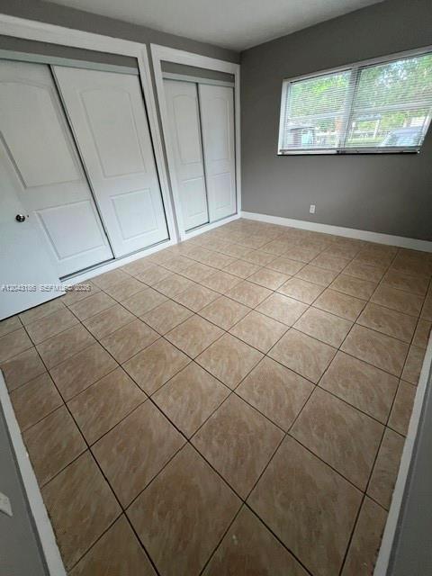 An empty bedroom features beige tile flooring, white walls, and two sets of closet doors — FORT LAUDERDALE, FL