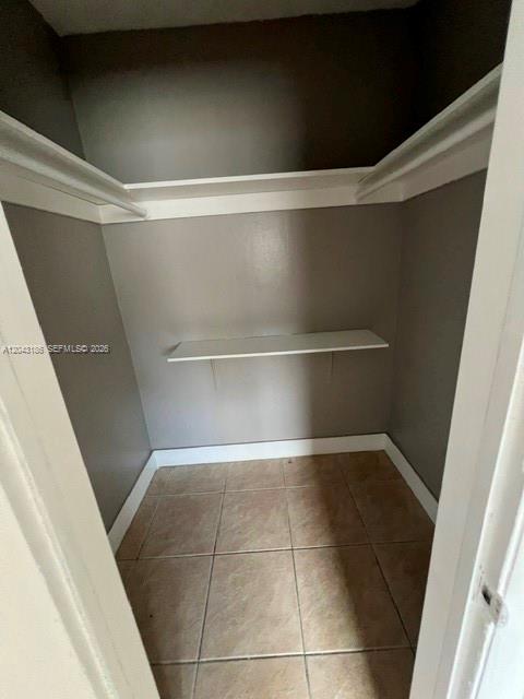 A small walk-in closet with beige tile flooring, gray walls, and two white shelves — FORT LAUDERDALE, FL