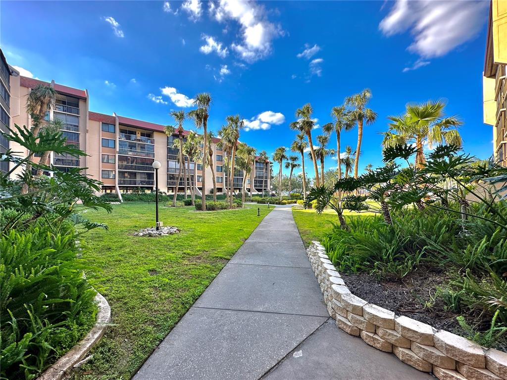 A concrete walkway leads through a landscaped courtyard between multi-story apartment buildings with palm trees — 3006 CARING WAY UNIT 529, PORT CHARLOTTE, FL