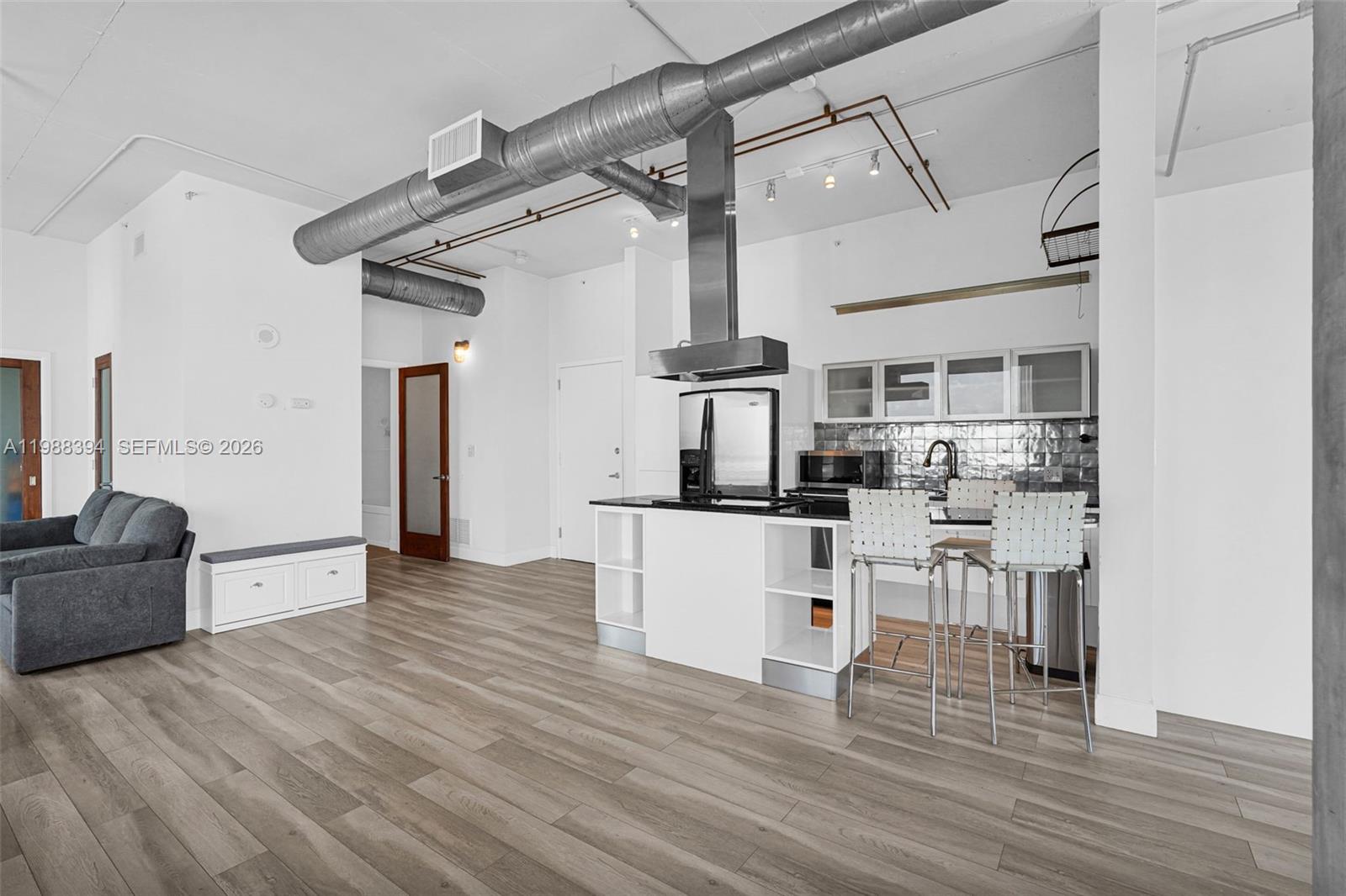 This open-concept kitchen and living area features industrial ductwork, wood-look flooring, and white cabinetry — 10 SW South River Dr # 1615, Miami FL 33130, MIAMI, FL