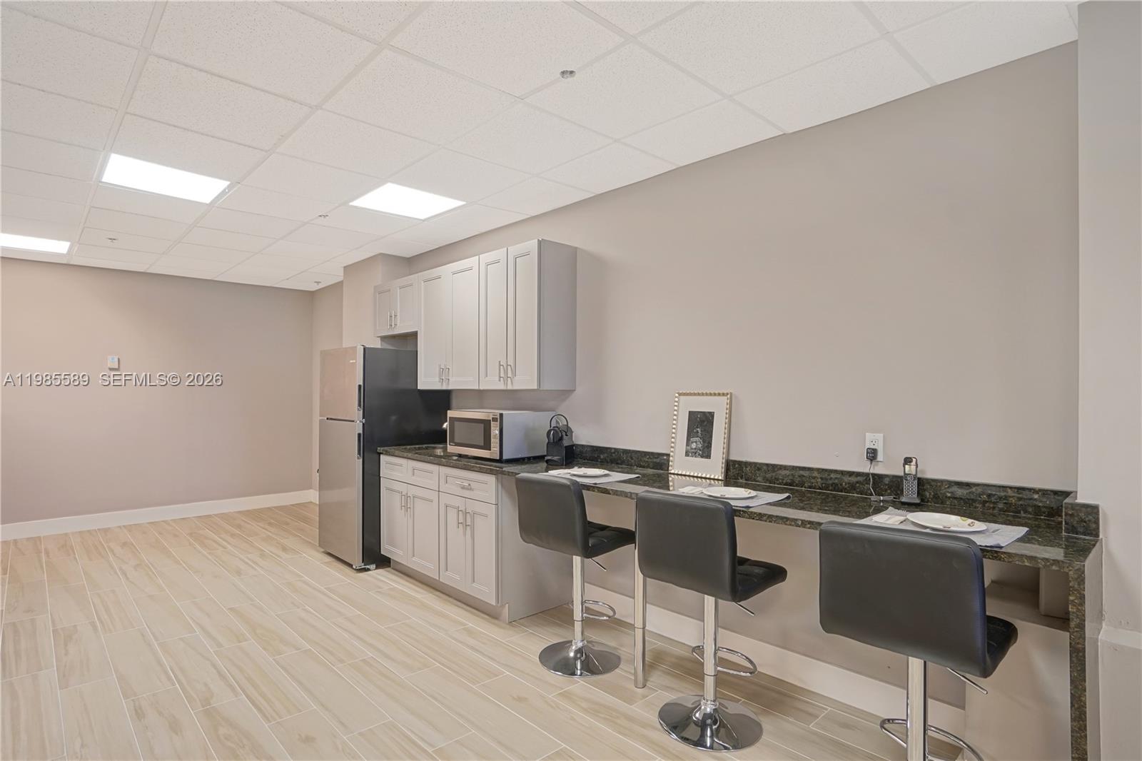 A kitchenette features gray cabinets, a stainless steel refrigerator, and a dark granite breakfast bar — 12550 Biscayne Blvd # 902, North Miami FL 33181, NORTH MIAMI, FL