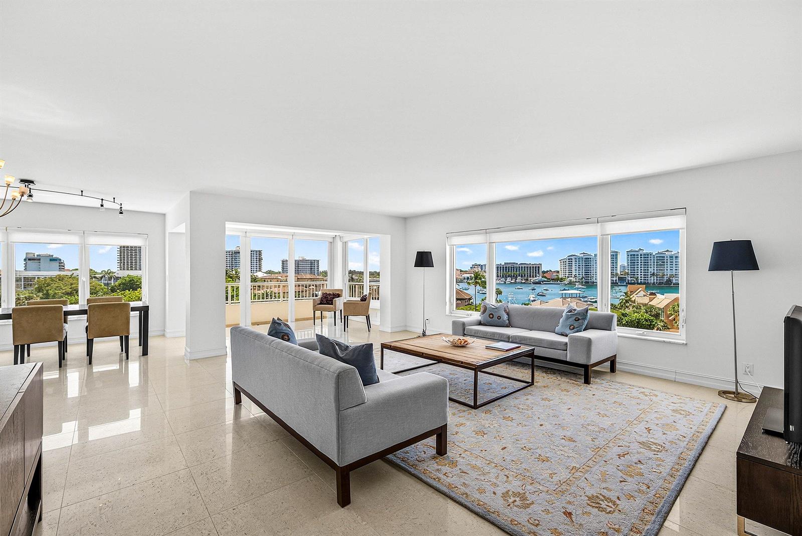 A bright living room with tile floors, two grey sofas, and large windows overlooking water — 600 S Ocean Boulevard # 504, Boca Raton FL 33432, BOCA RATON, FL