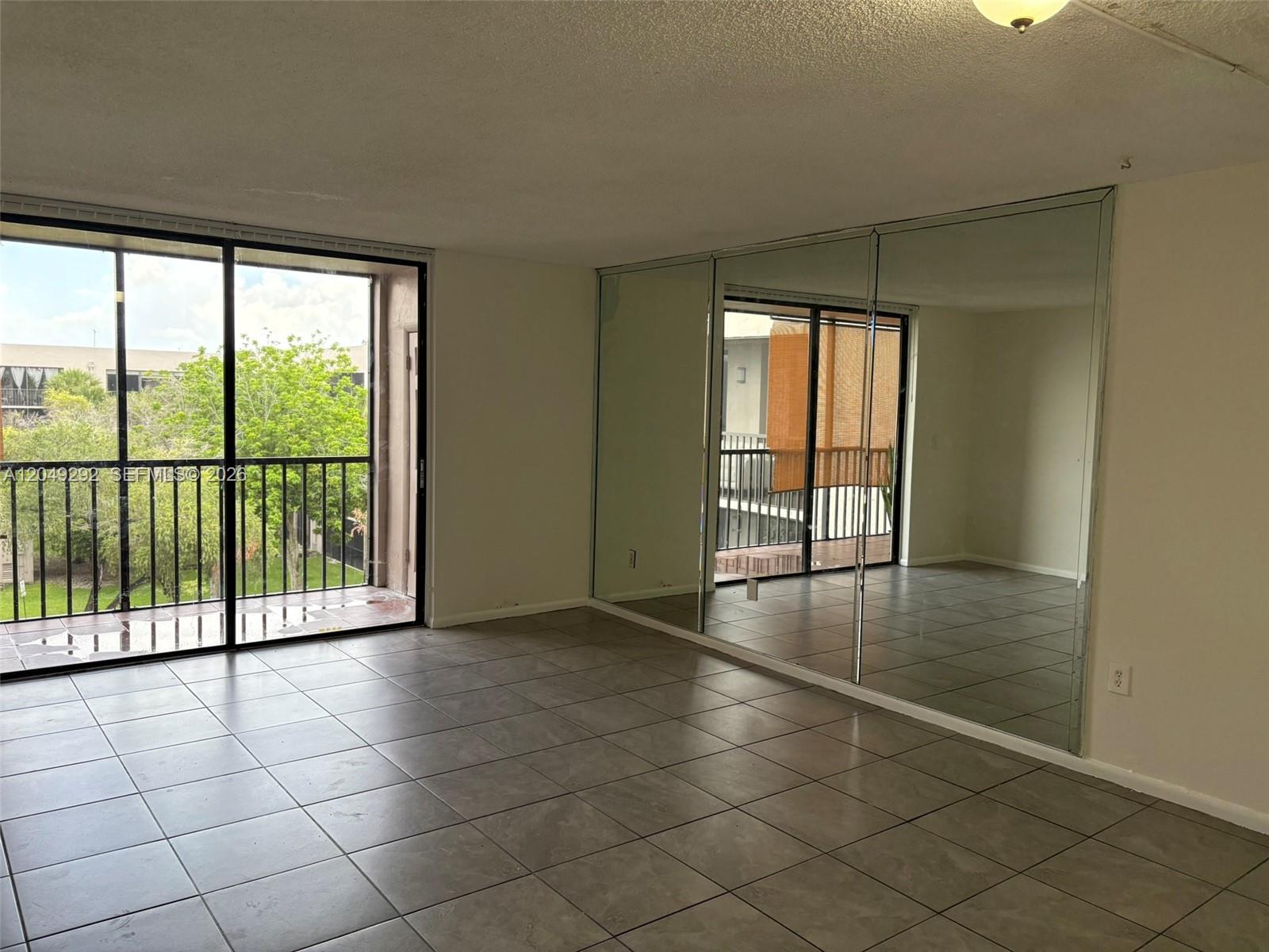 An empty room features gray tile flooring, a sliding glass balcony door, and mirrored walls — 8500 SW 133rd Ave Rd # 422, Miami FL 33183, MIAMI, FL