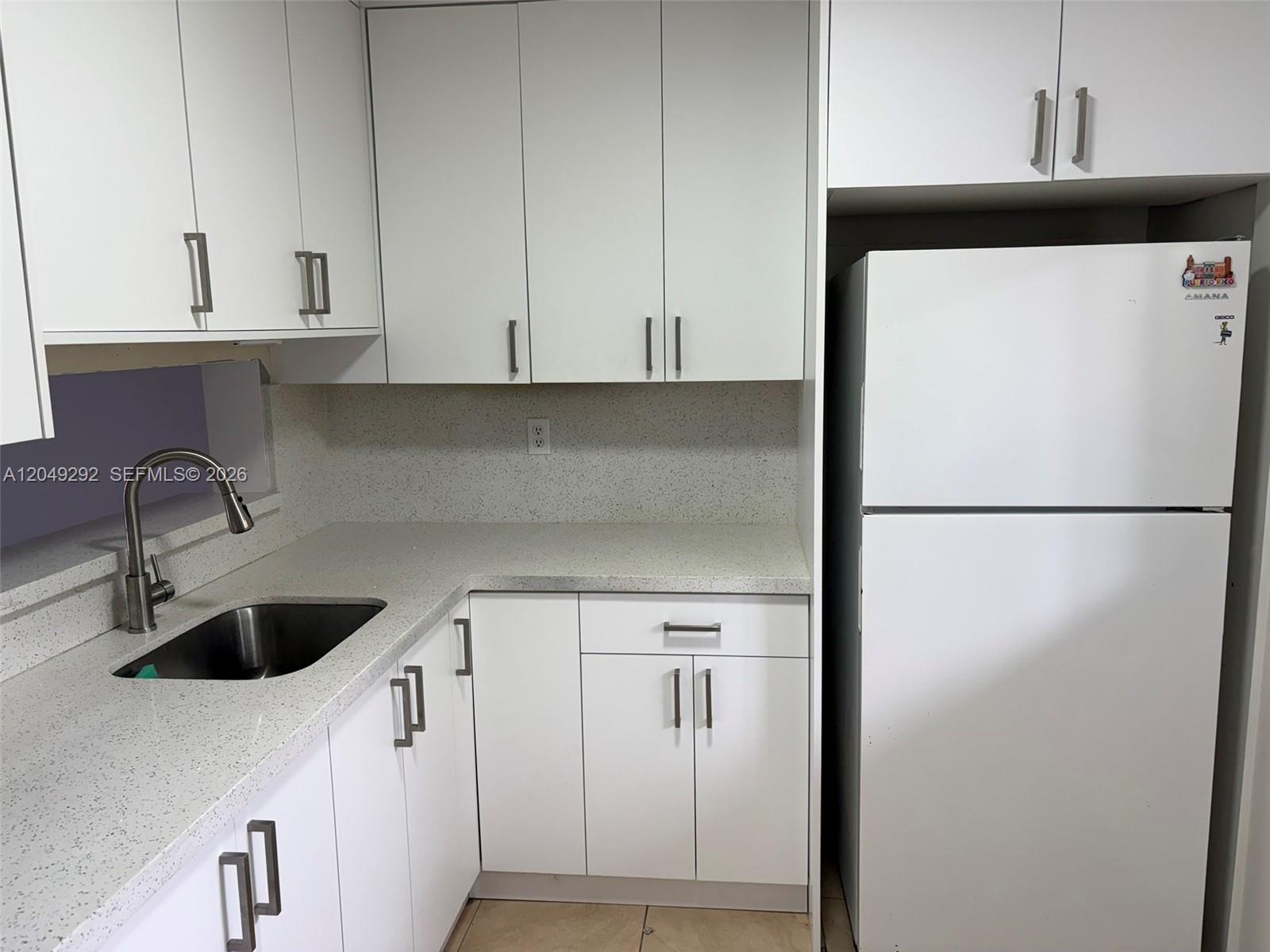 A kitchen features white cabinets, a stainless steel sink, and speckled countertops next to a refrigerator — 8500 SW 133rd Ave Rd # 422, Miami FL 33183, MIAMI, FL