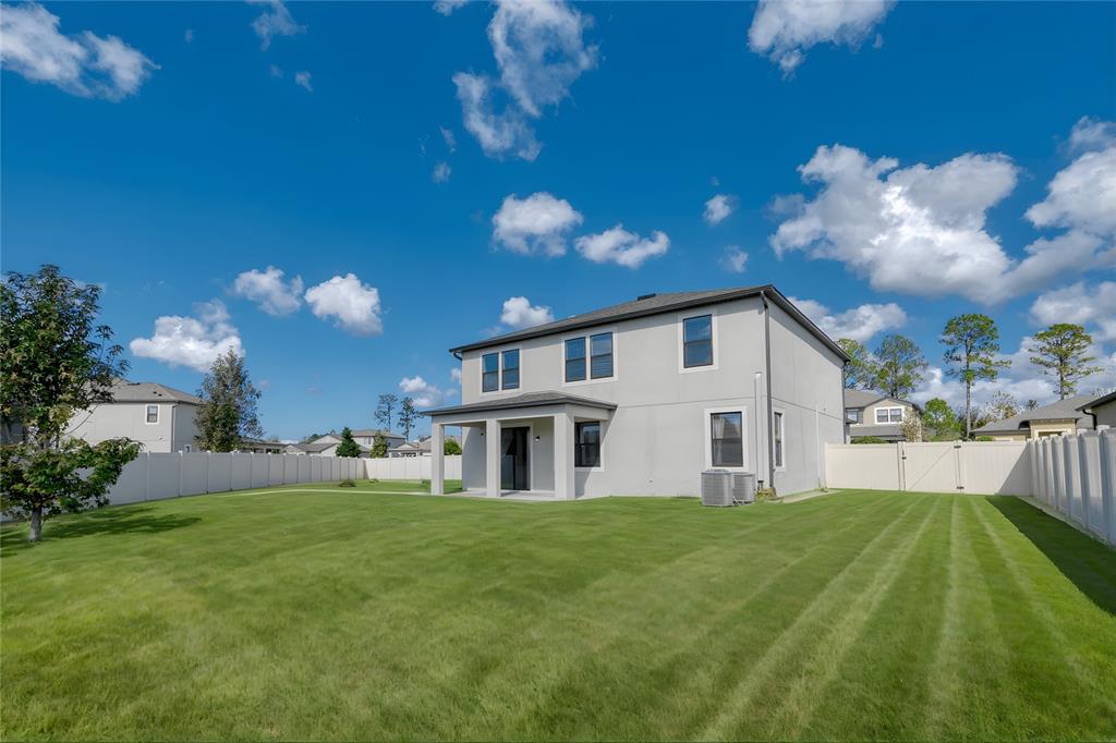 The backyard of a two-story house features a covered patio and a white vinyl fence — 18576 OBREGAN DRIVE, SPRING HILL, FL