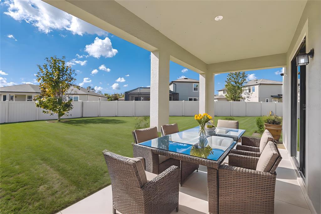 A covered patio features a glass-topped dining set overlooking a fenced backyard with green grass — 18576 OBREGAN DRIVE, SPRING HILL, FL