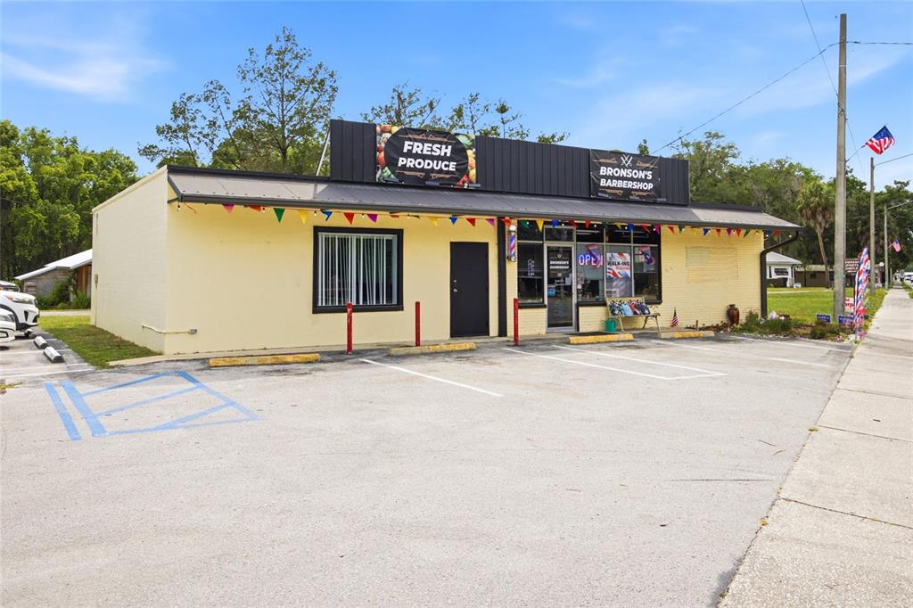 A single-story commercial building with a yellow exterior features a barbershop and produce store signage — 380 E HATHAWAY AVENUE, BRONSON, FL
