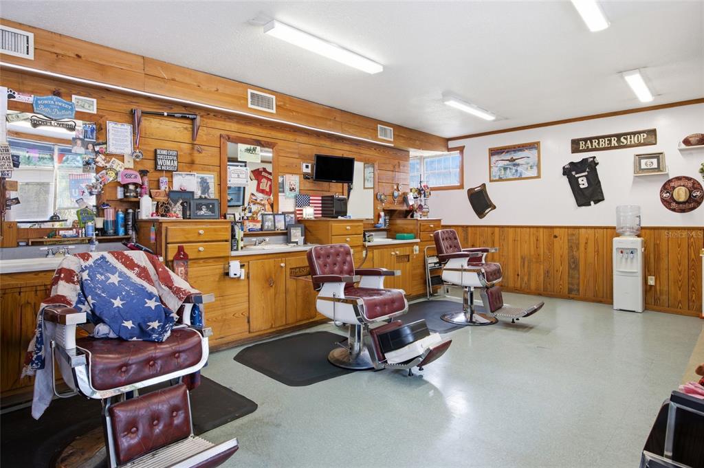 A barbershop interior features three vintage leather chairs, wood-paneled walls, and fluorescent ceiling lights — 380 E HATHAWAY AVENUE, BRONSON, FL