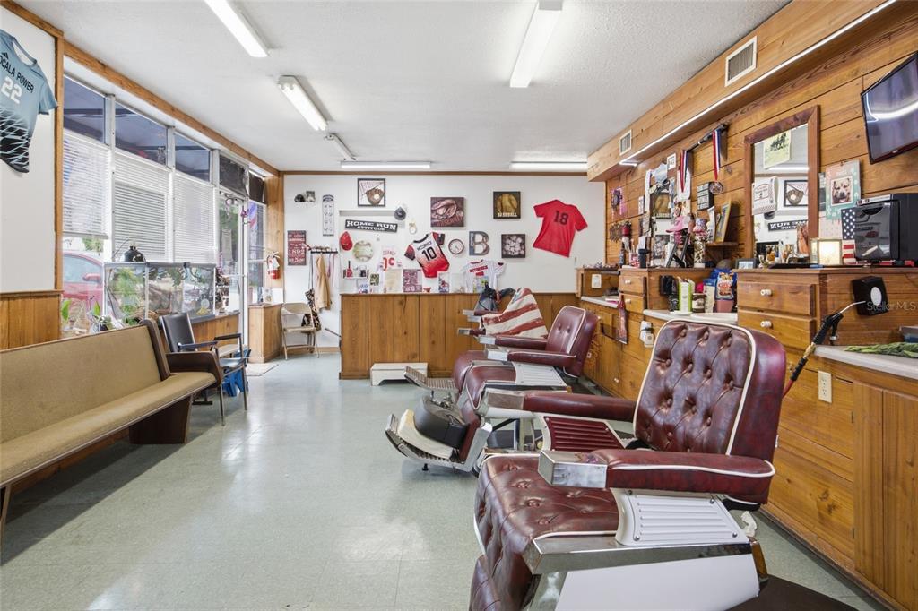 A barbershop interior features two red leather chairs, wood-paneled walls, and sports-themed decor — 380 E HATHAWAY AVENUE, BRONSON, FL