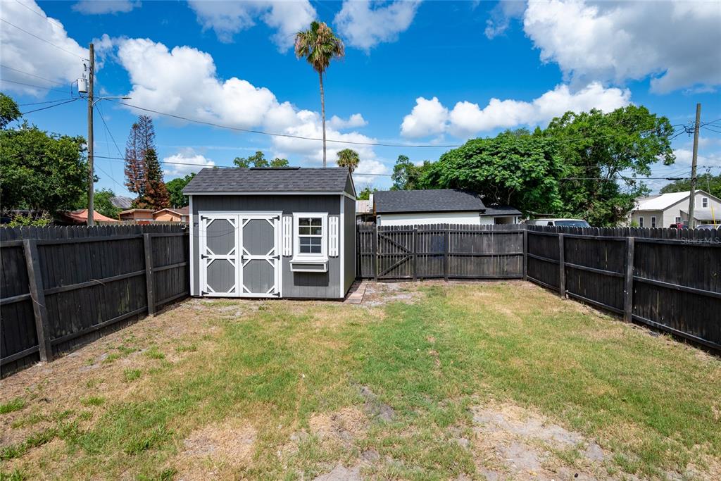 A gray storage shed sits in a fenced backyard under a blue sky — 922 DELAWARE AVENUE, ST CLOUD, FL