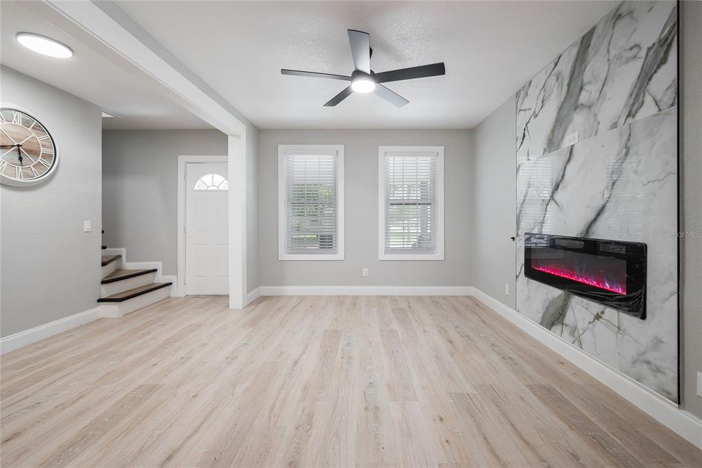 A living room features light wood flooring, a marble-tiled fireplace wall, and a ceiling fan — 922 DELAWARE AVENUE, ST CLOUD, FL