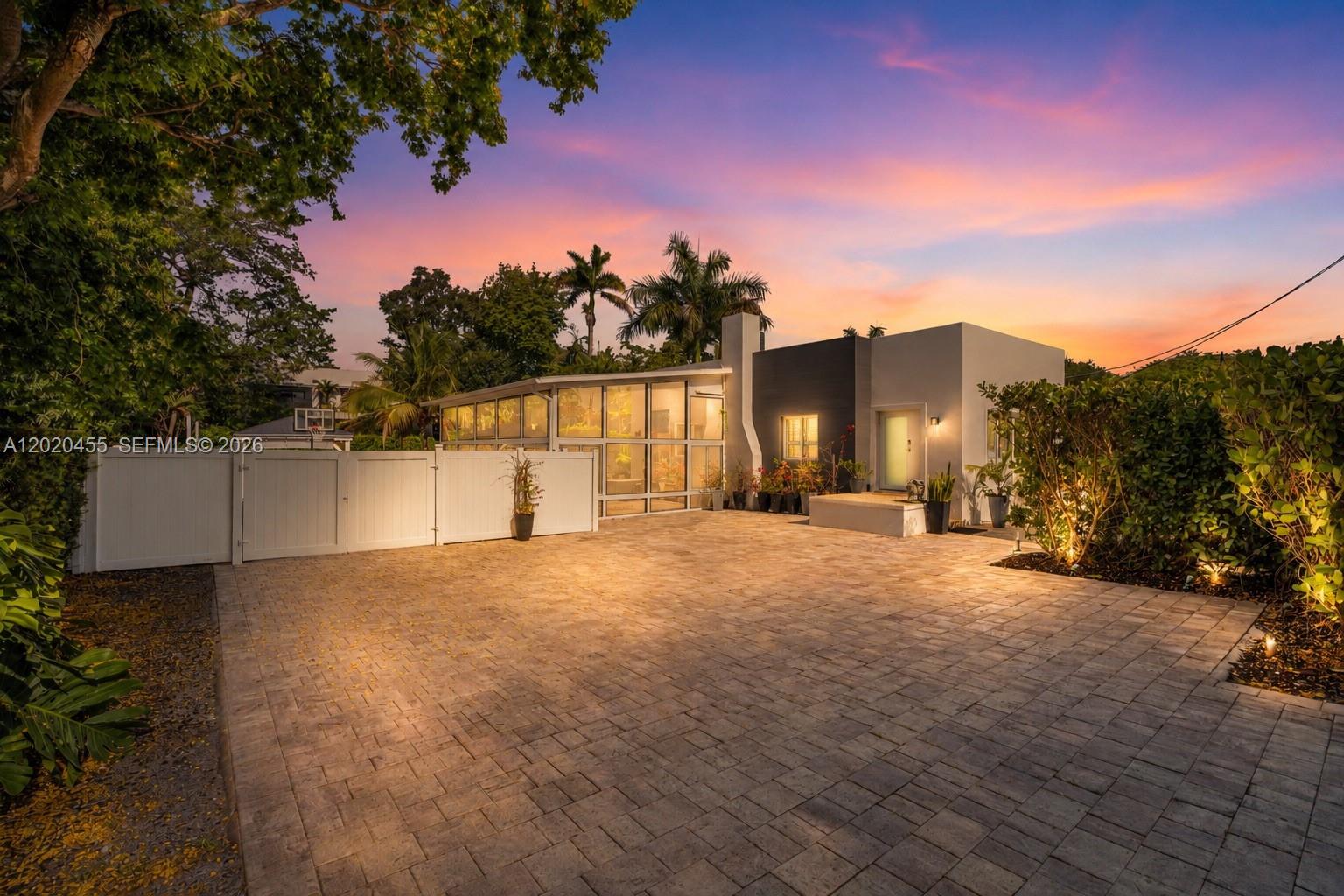 A modern house with a glass-enclosed room and a paved driveway at sunset — 11144 NE 8th Ct, Biscayne Park FL 33161, BISCAYNE PARK, FL