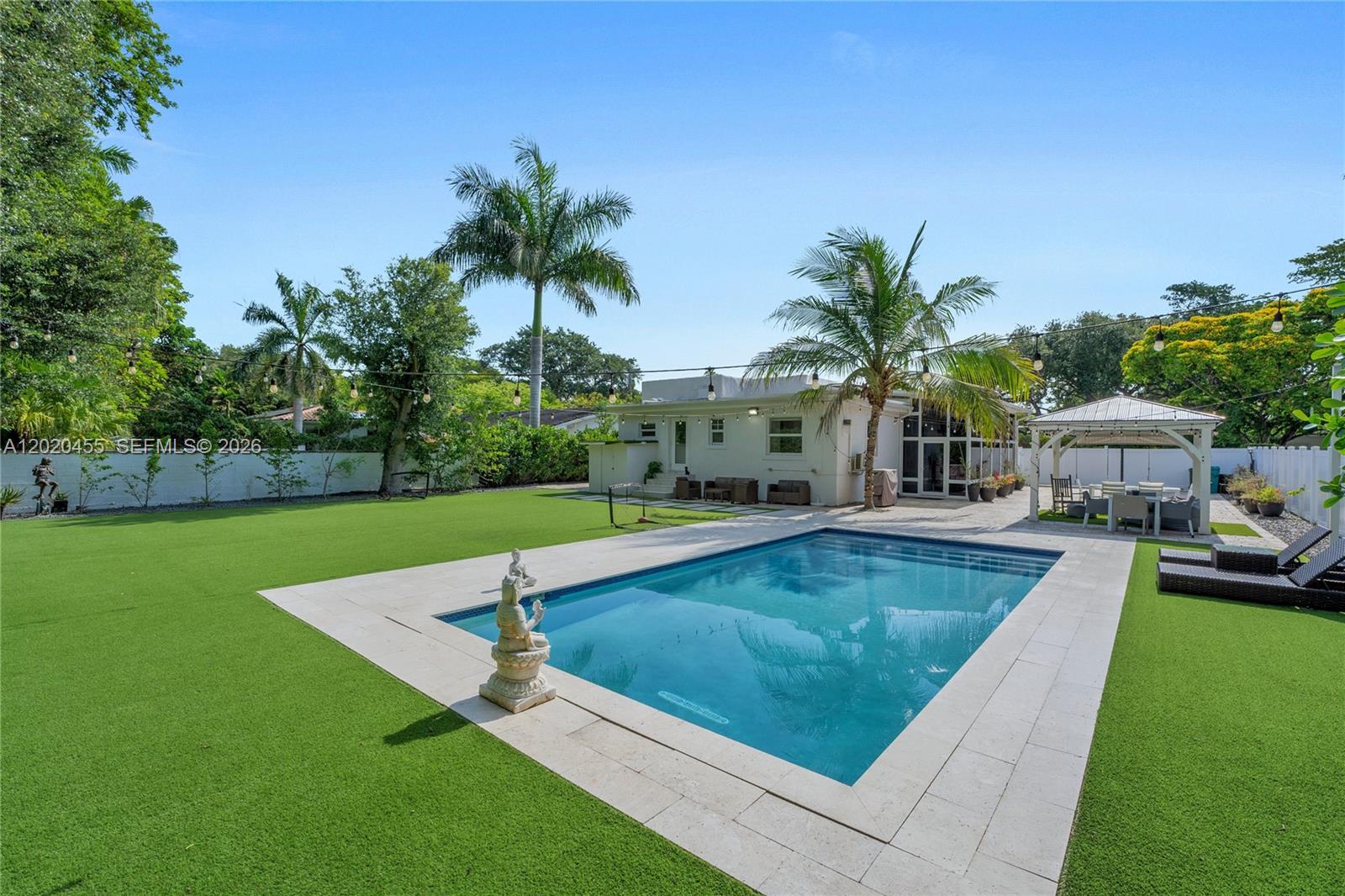 A backyard features a rectangular swimming pool, artificial turf, a gazebo, and string lights — 11144 NE 8th Ct, Biscayne Park FL 33161, BISCAYNE PARK, FL