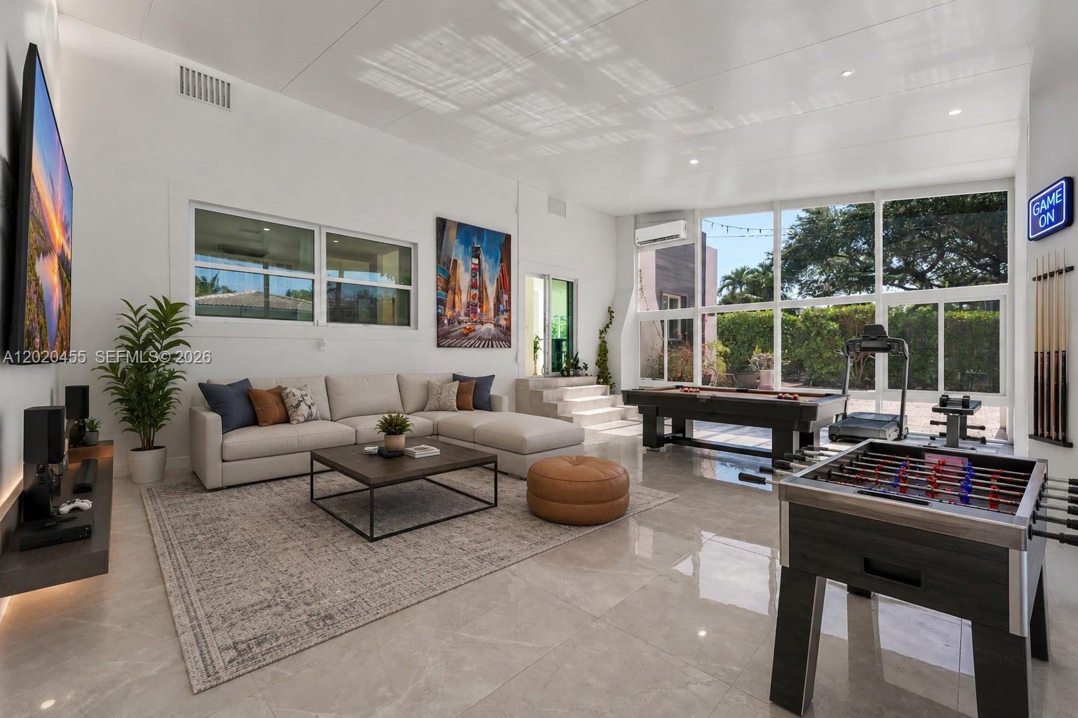 A spacious game room features a sectional sofa, pool table, foosball table, and large windows — 11144 NE 8th Ct, Biscayne Park FL 33161, BISCAYNE PARK, FL