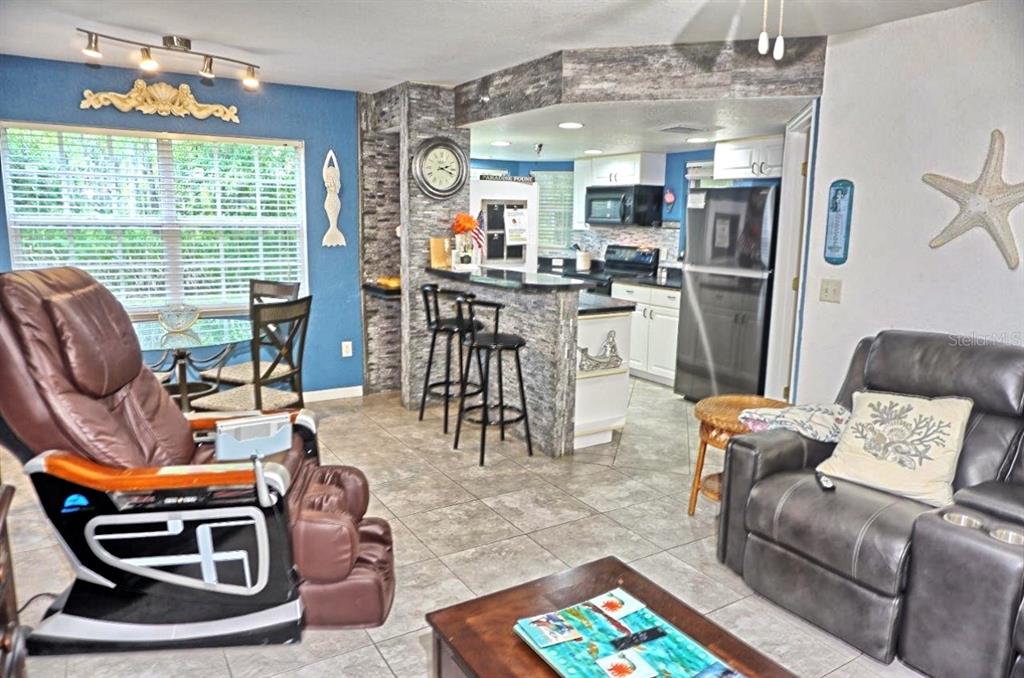 A living room with tile floors, a stone-accented kitchen bar, and a brown recliner — 21107 FOUNTAIN VIEW LANE UNIT 5102, LUTZ, FL