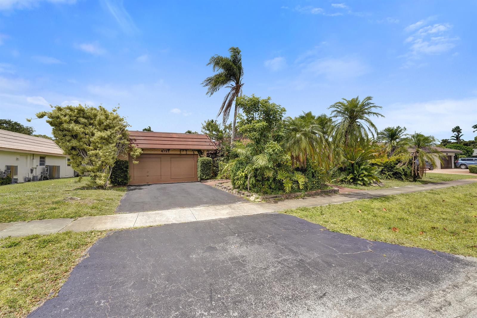 A single-story house with a brown garage door and lush landscaping under a blue sky — 4721 Sarazen Drive, Hollywood FL 33021, HOLLYWOOD, FL