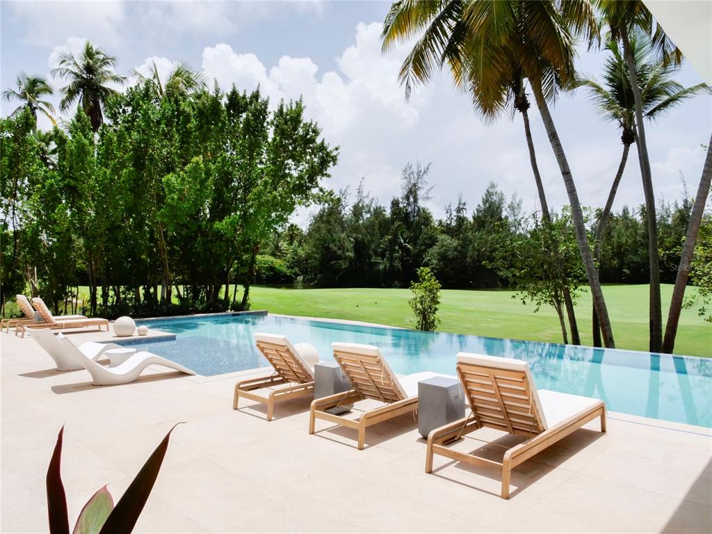 A swimming pool with lounge chairs overlooks a grassy lawn and palm trees — 7000 BAHIA BEACH G3 ATLANTIC DRIVE, RIO GRANDE, PR