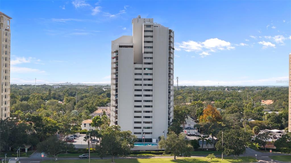 A tall, white residential high-rise building stands surrounded by trees and a parking area — 4141 BAYSHORE BOULEVARD UNIT 1702, TAMPA, FL