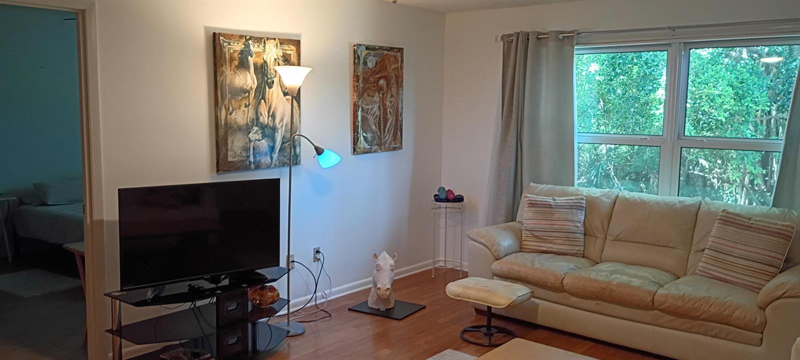 A living room features a beige leather sofa, a television on a stand, and artwork — 8387 SE Croft Circle # Q3, Hobe Sound FL 33455, HOBE SOUND, FL