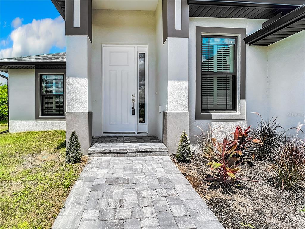 A paved walkway leads to the white front door of a modern house with stucco siding — 14267 MONTMARTE AVENUE, PORT CHARLOTTE, FL