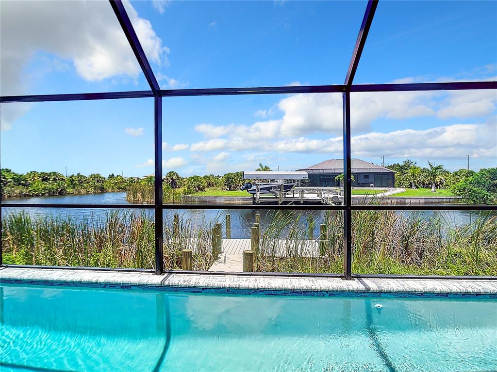 A swimming pool sits in front of a screened-in patio overlooking a canal and dock — 14267 MONTMARTE AVENUE, PORT CHARLOTTE, FL