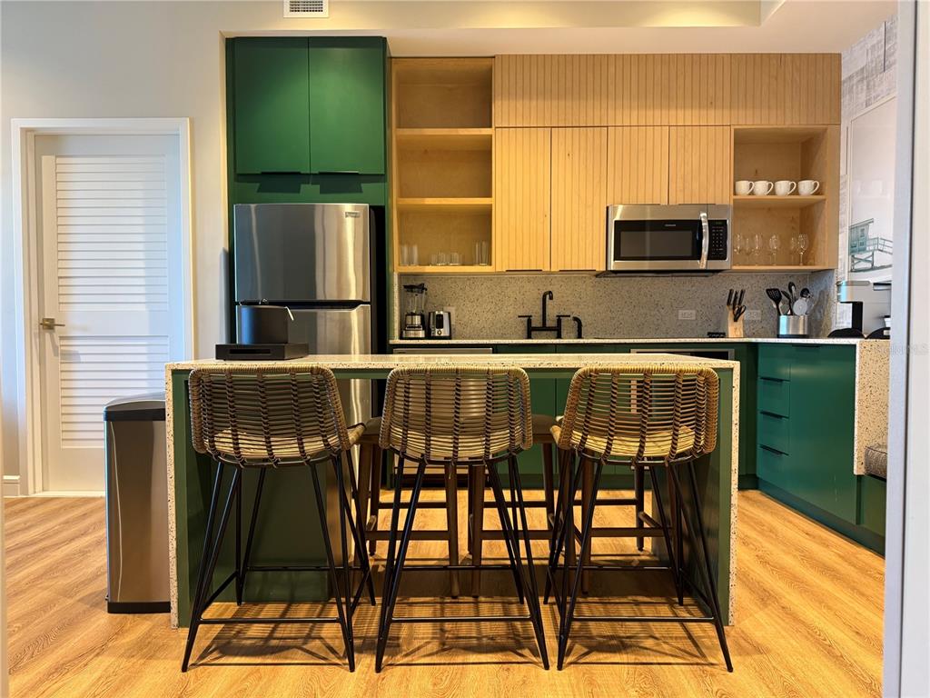 A kitchen features a green island with three woven stools, light wood cabinets, and stainless appliances — 3151 SUNSET WALK DRIVE UNIT 212, KISSIMMEE, FL