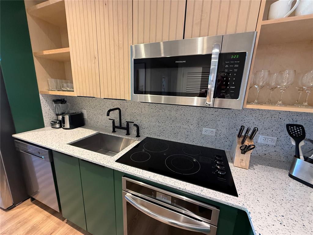 A modern kitchen features green lower cabinets, light wood upper cabinets, and speckled countertops — 3151 SUNSET WALK DRIVE UNIT 212, KISSIMMEE, FL