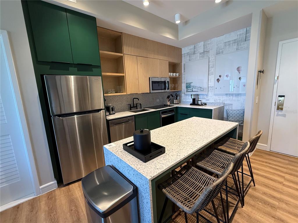 A modern kitchen features green cabinets, light wood accents, a speckled island, and stainless appliances — 3151 SUNSET WALK DRIVE UNIT 212, KISSIMMEE, FL