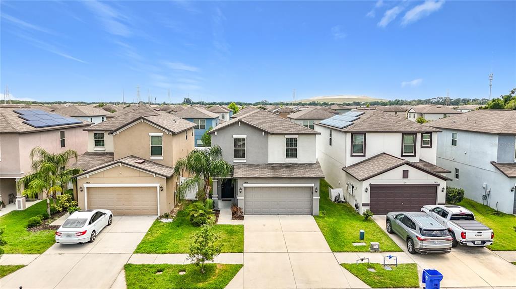 An aerial view shows three suburban houses with driveways and lawns under a blue sky — 7405 EVENING PRIMROSE COURT, TAMPA, FL