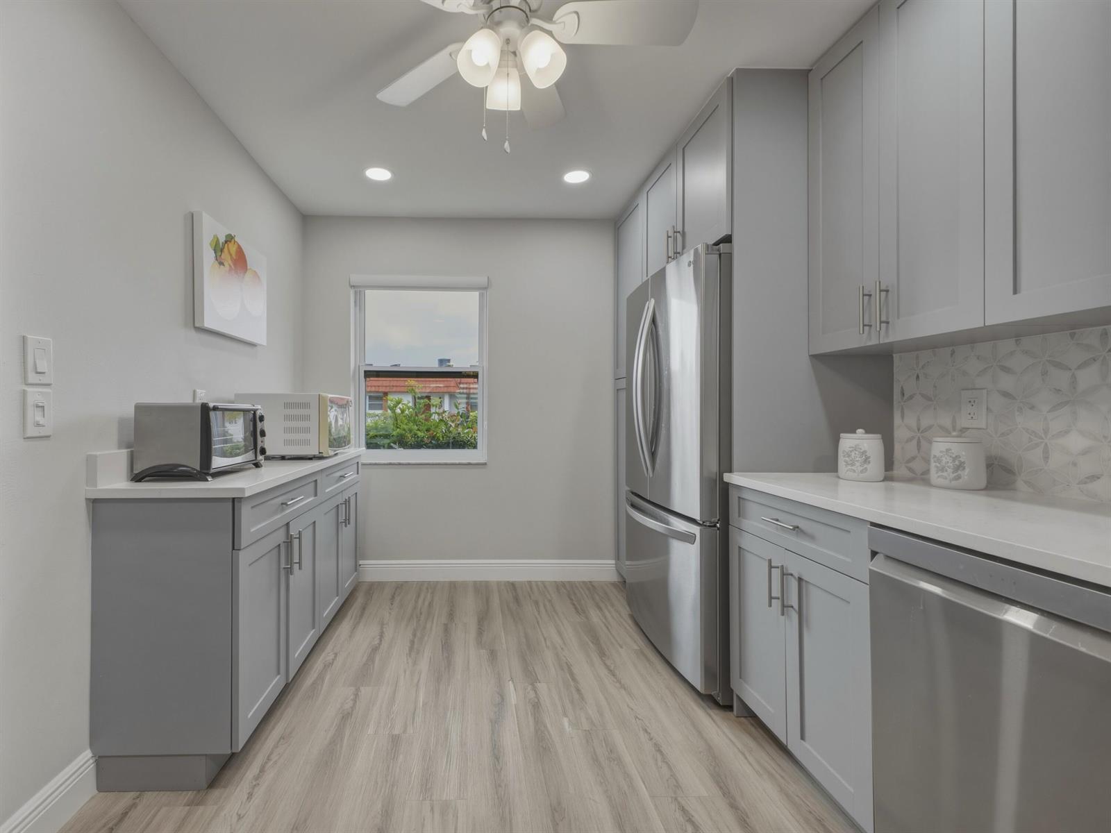 A galley kitchen features gray cabinets, stainless steel appliances, white countertops, and light wood flooring — 5800 W Fernley Dr W # 9, FL 33415, FL