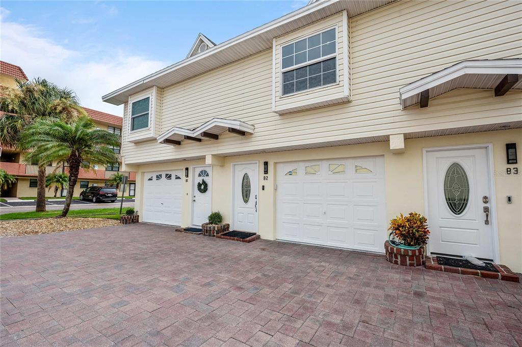 The exterior of a two-story townhouse complex features beige siding, white garage doors, and brick pavers — 19651 GULF BOULEVARD UNIT B2, INDIAN SHORES, FL