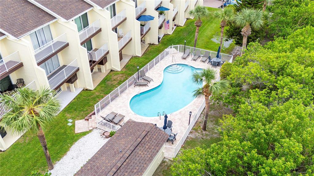 An aerial view shows a multi-story apartment building next to a swimming pool and trees — 19651 GULF BOULEVARD UNIT B2, INDIAN SHORES, FL