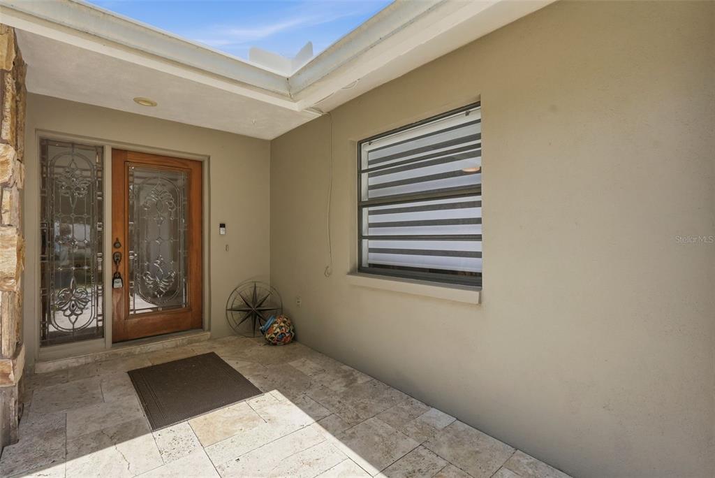 A covered entryway features a wooden front door with glass inserts and stone tile flooring — 707 KNOLLWOOD DRIVE, LARGO, FL